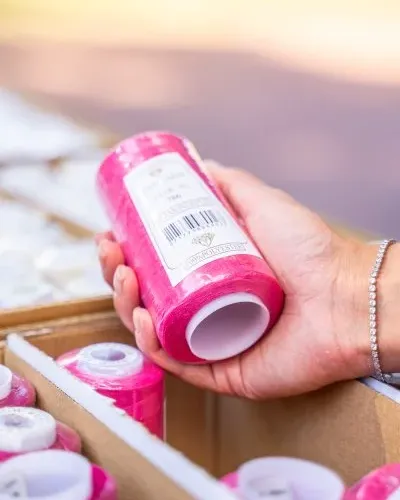 Hand hält pinke Nähgarnrolle über Garnkiste